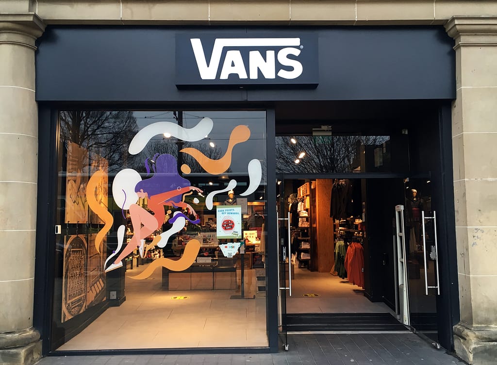 A photo of a Vans Edinburgh store window displaying an illustration of a woman mid-jump, surrounded by vibrant yellow and white blobs, promoting the "Make It Special" campaign.
